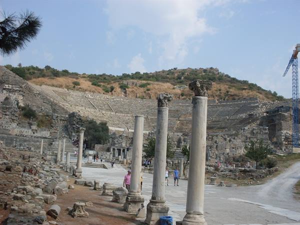 Marble columns and amphitheater ruins at Ephesus under cloudy sky, tourists walking