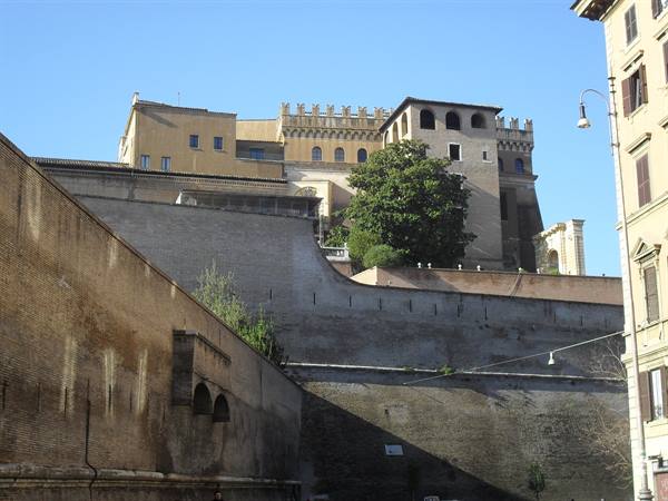 Vatican brick walls under blue sky, crenellated palace and green tree