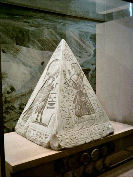 Limestone pyramidion with hieroglyphs and deities displayed behind glass in a museum