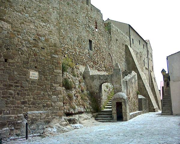 Ancient stone walls with arch, stairs and empty cobblestone street