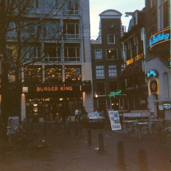Burger King and Bulldog neon signs among Dutch gabled houses, dusk square