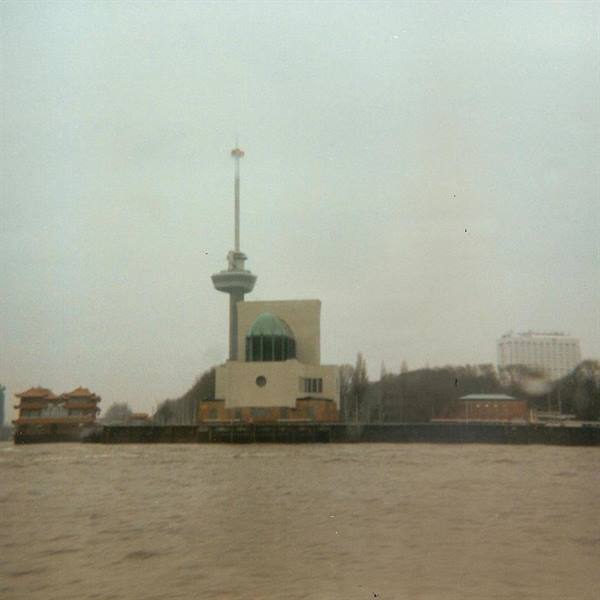 Euromast tower above a green-domed pavilion, seen from the river under grey sky