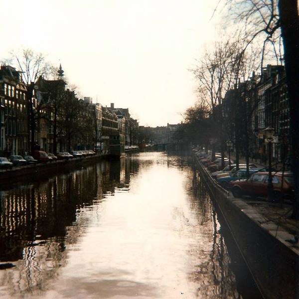 Amsterdam canal, parked cars along the embankment, narrow houses and bare trees