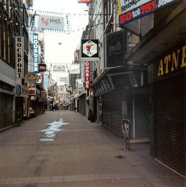 Pedestrian street with shop signs and closed shutters under grey light