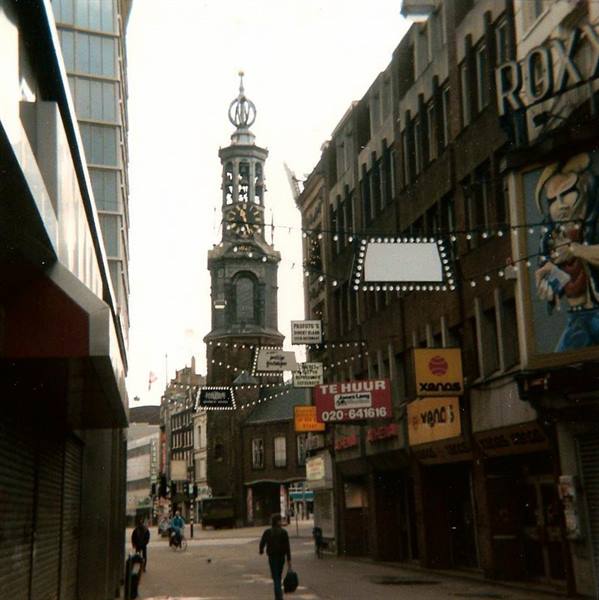 The Munttoren towering over an Amsterdam shopping street with storefronts and light garlands