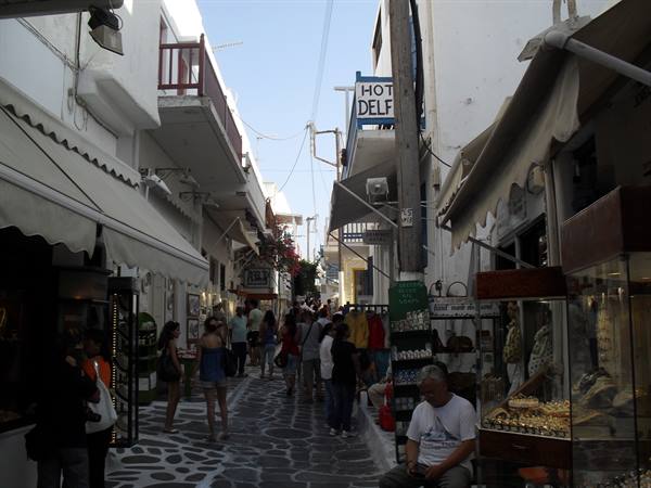 Shoppers in a paved whitewashed alley with shops and blue signs, Mykonos