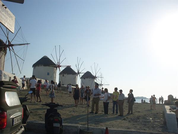 Tourists in front of Mykonos white windmills under late afternoon sun