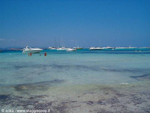 Boats anchored in clear turquoise water, swimmers on the sandy beach
