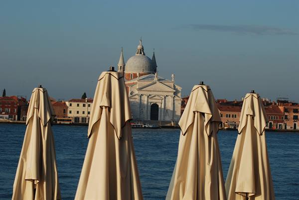 Closed beach umbrellas over the lagoon, Redentore church in the background, Venice