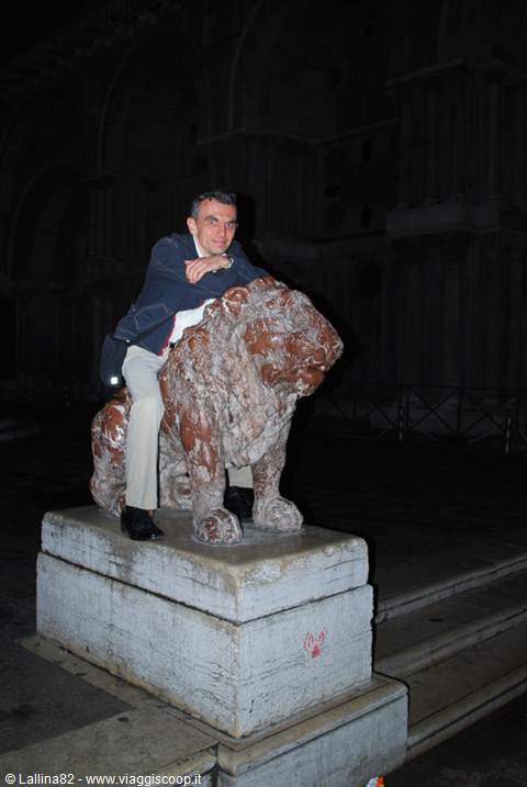 Tourist in blue jacket riding a stone lion statue at night