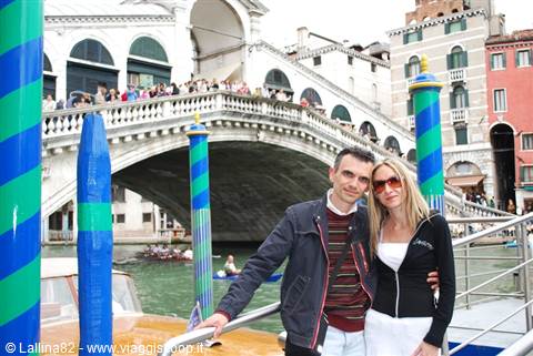 Couple in front of Rialto Bridge in Venice, striped poles and busy canal