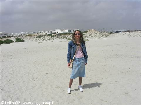 Girl in denim jacket on a white sand beach with dunes and houses