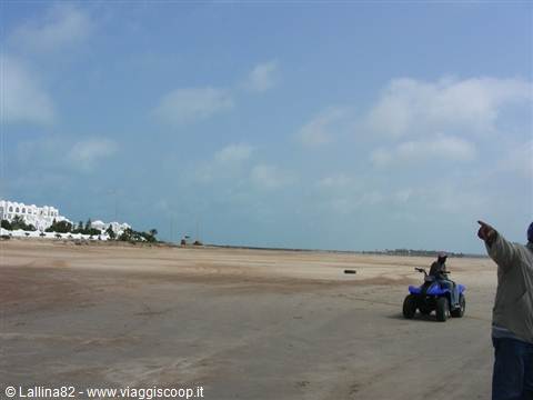 Quad bike on sandy beach, man pointing the way, white building behind