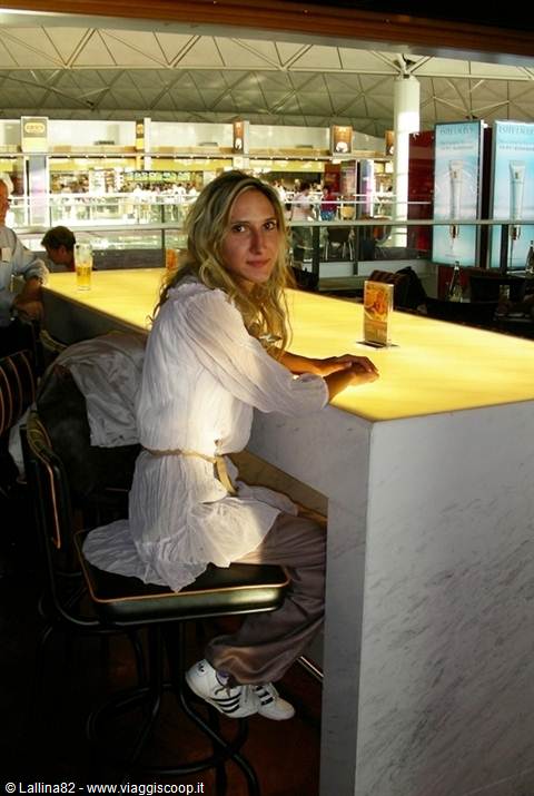 Blonde woman in white blouse at the glowing airport bar, Hong Kong
