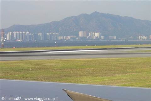 Airplane wing landing, green runway and skyscrapers beneath Hong Kong mountains