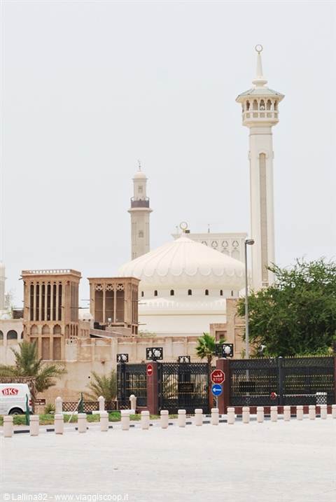 White mosque minaret and dome beside coral stone houses in Bastakia quarter