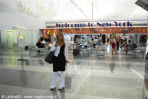 Smiling woman with bag at JFK airport, Welcome to New York sign