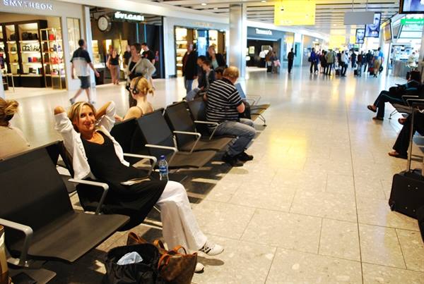 Woman sitting among metal seats in airport waiting area with shops and travelers