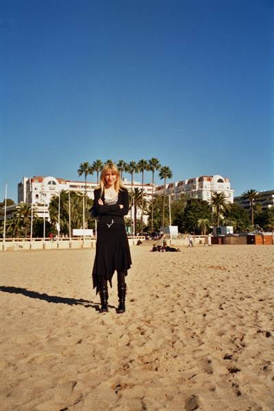 Woman in black standing on sand, palms and white hotels behind