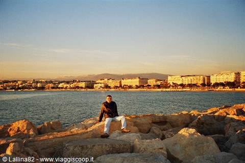Man sitting on rocks by the bay, seafront buildings in warm evening light