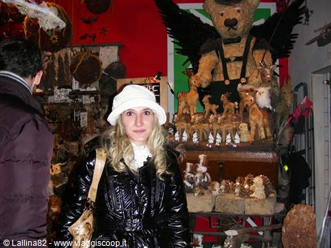 Woman in white hat at a Christmas stall with winged teddy bear and wooden figurines