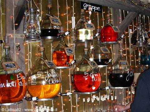 Demijohns filled with colorful grappa hanging among fairy lights at Christmas market