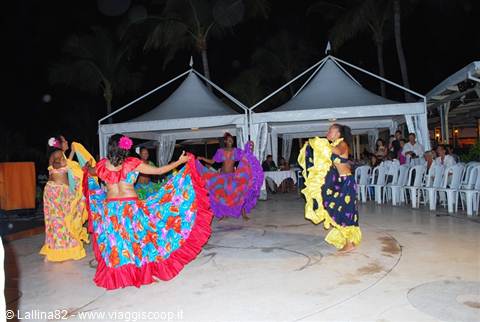 Dancers in colorful ruffled dresses perform at night before white tents