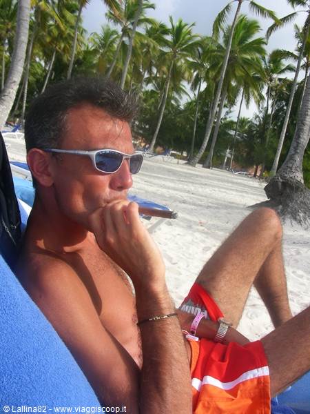 Man in sunglasses smoking a cigar on a lounge chair among palm trees
