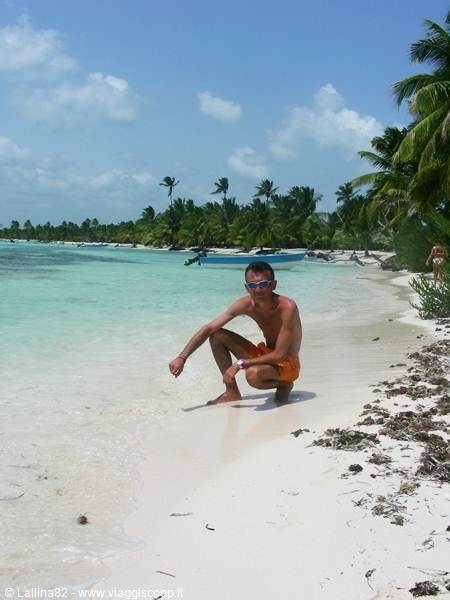 Man crouching on white sand beach, palm trees and motorboat along the shore