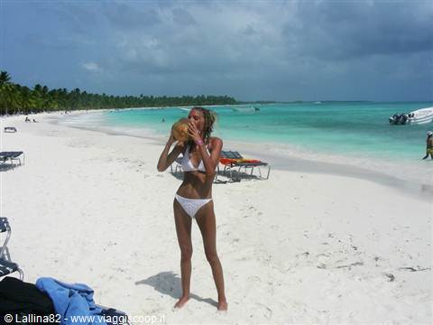 Woman in bikini drinking from a coconut on white sand beach, turquoise sea, boat