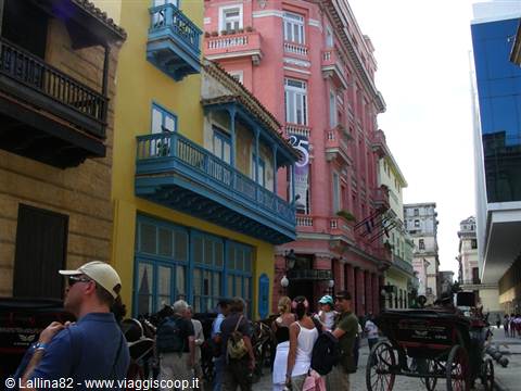Tourists and horse carriage beside colorful colonial buildings with wooden balconies in Havana