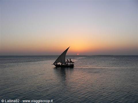 Dhow with triangular sail glides at dusk, dark silhouette on calm sea