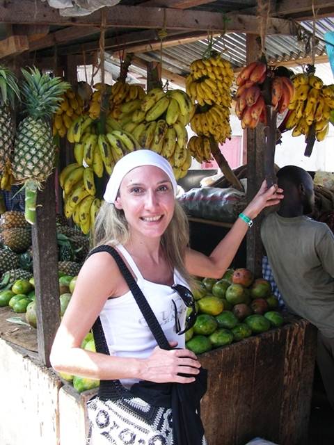 Smiling tourist beside hanging bananas and pineapples at a wooden fruit stall