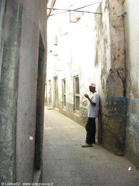 Man leaning on a weathered wall in a narrow Stone Town alley