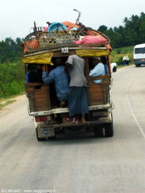 Passengers riding on the back of an overloaded old truck on a rural road