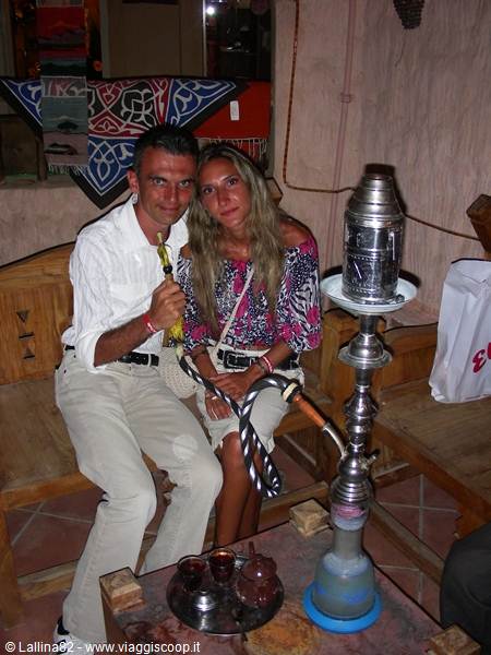 Smiling couple on wooden bench beside a large metal shisha pipe