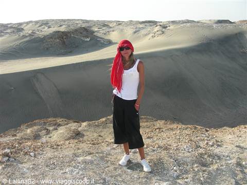 Woman with red scarf standing on rock in front of sand dunes