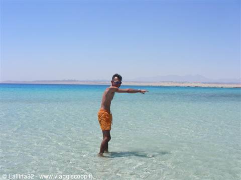 Boy in orange swim shorts points at the horizon in clear turquoise water