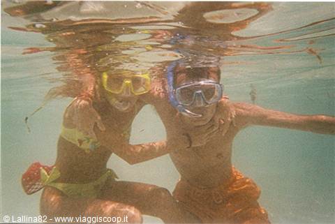 Two teenagers in snorkel masks hugging underwater in clear turquoise sea
