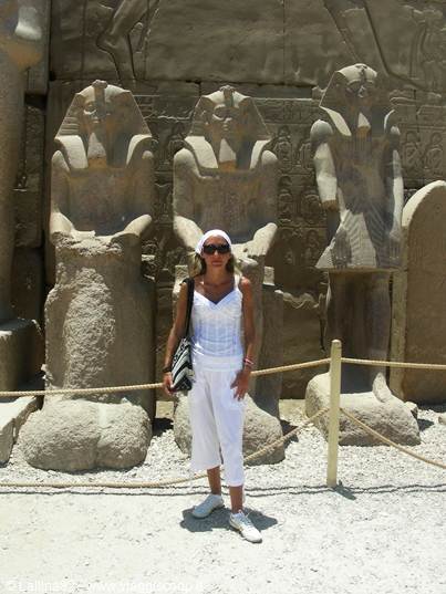 Tourist in white posing before sandstone pharaoh statues under the sun