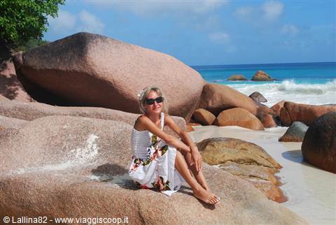 Woman in white dress sitting on pink granite rocks by turquoise waves