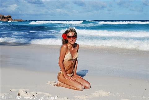Woman in bikini kneeling on white sand in front of breaking waves