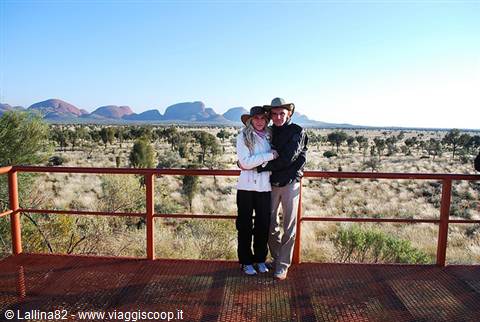 Couple in hats on the red metal platform facing Kata Tjuta