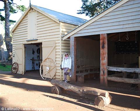Woman in white jacket beside pale wooden barns with old wheels and tools