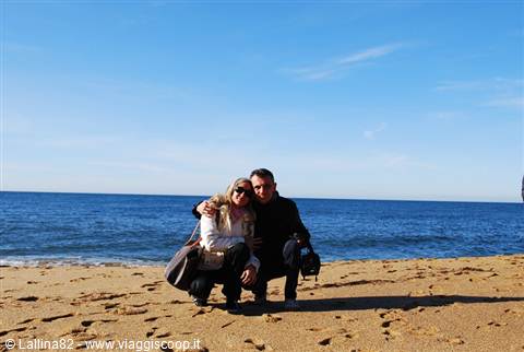 Couple crouching on sandy beach in front of blue sea
