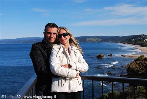 couple hugging on a railing terrace overlooking sunny bay and beach