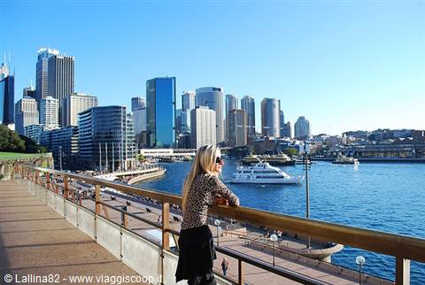 Blonde woman leaning on railing overlooking Circular Quay, Sydney, with skyscrapers and ferry