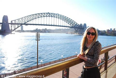 Blonde woman with sunglasses leaning on railing, Sydney Harbour Bridge behind