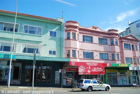Pastel-colored buildings at Bondi Beach, white car parked in front of shops
