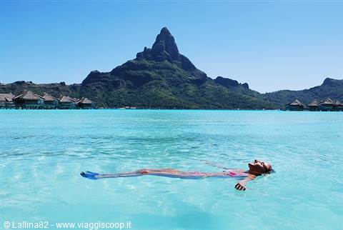 Woman floating on Bora Bora's turquoise lagoon, Mount Otemanu and overwater bungalows behind